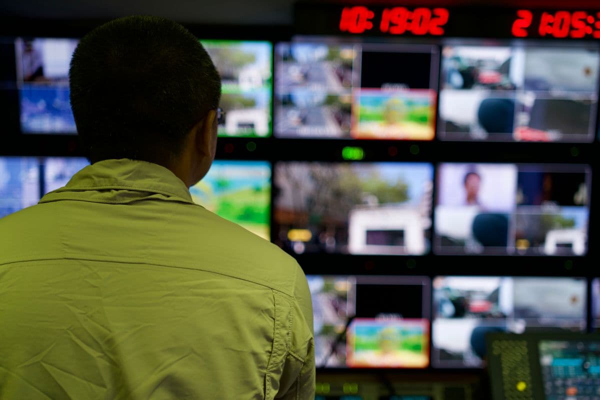 A broadcast control room wall of monitors, seen from behind